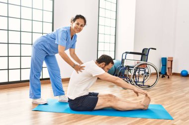 Orta yaşlı bir adam ve kadın fizyoterapi kliniğinde rehabilitasyon seansı yaparken gülümsüyor.