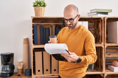 Genç bir iş adamı. Ofiste elinde bir panoyla kahve içiyor.