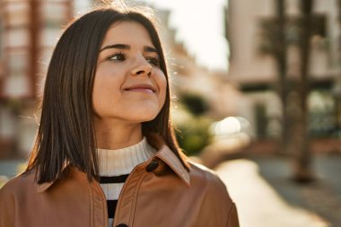 Genç, güzel, esmer kadın dışarıda mutlu bir şekilde gülümsüyor.