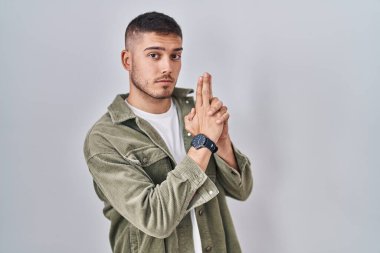 İspanyol genç adam izole edilmiş arka planda duruyor. Elinde sembolik bir silah var. El hareketleriyle cinayet silahlarıyla oynuyor. 