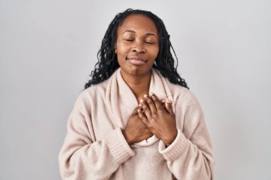 African woman standing over white background smiling with hands on chest with closed eyes and grateful gesture on face. health concept. 