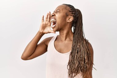 Black woman with braids standing over isolated background shouting and screaming loud to side with hand on mouth. communication concept. 