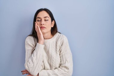 Mavi arka planda duran esmer kadın kollarını kavuşturarak depresyondan sıkılmış ve yorgun görünüyor.. 