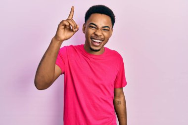 Casua tişörtü giymiş genç Afro-Amerikan bir adam başarılı bir fikri işaret ediyor. Heyecanlı ve mutlu. Bir numara.. 