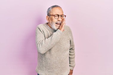 Handsome senior man with beard wearing casual sweater and glasses hand on mouth telling secret rumor, whispering malicious talk conversation 