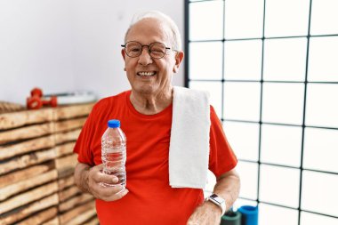 Senior man wearing sportswear and towel at the gym winking looking at the camera with sexy expression, cheerful and happy face. 