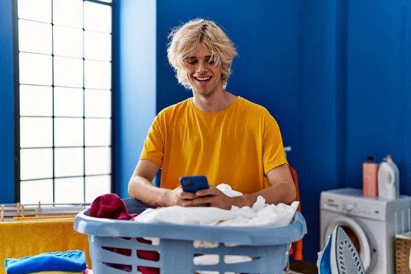 Genç Sarışın Adam Çamaşır Odasında Çamaşır Sepetine Yaslanmış Akıllı Telefon — Stok fotoğraf