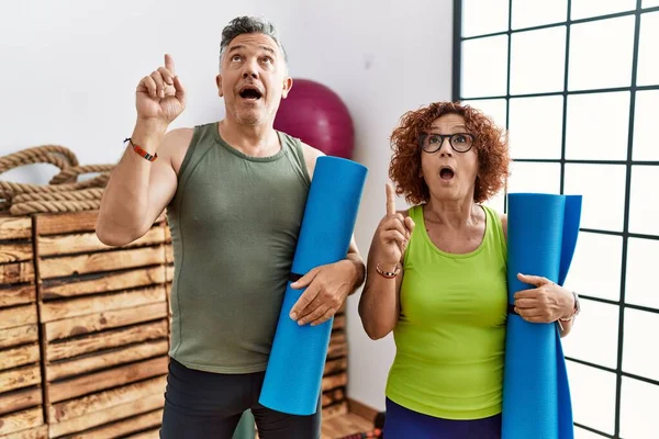 Middle Age Couple Holding Yoga Mat Amazed Surprised Looking Pointing — ストック写真