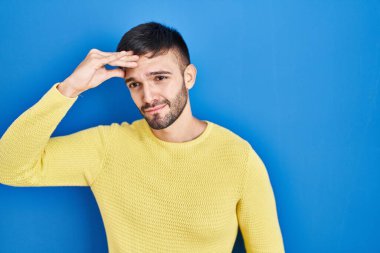 Mavi arka planda dikilen İspanyol adam, alnındaki bir sorunla ilgili endişeli ve stresli, gergin ve kriz için endişeli. 