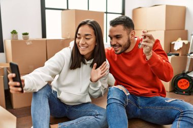 Genç Latin çift gülümsüyor. Yeni evlerinde akıllı telefon kullanarak video araması yapıyorlar..