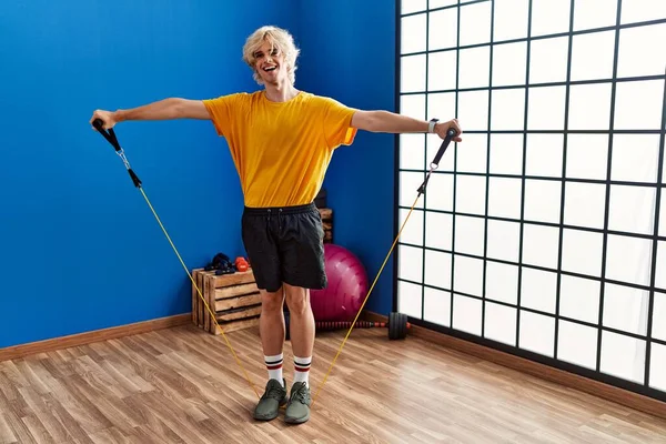 Young blond man smiling confident using elastic band training at sport center