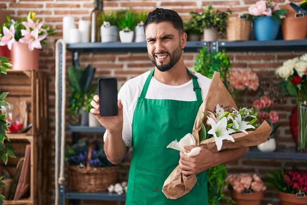 スマートフォンの画面を表示する花屋の店で働いているヒスパニック系の若者は無知で混乱した表情 疑わしい概念 — ストック写真