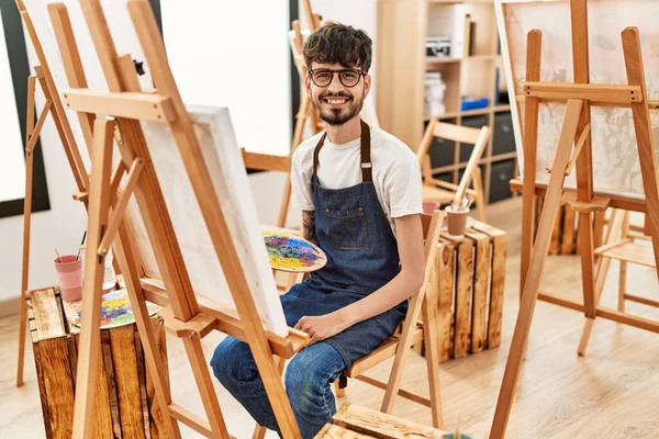Hispanic man with beard at art studio looking positive and happy standing and smiling with a confident smile showing teeth