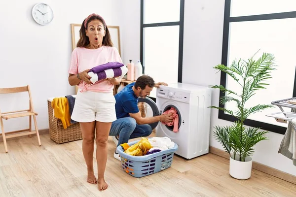 Middle Age Couple Holding Clean Laundry Scared Amazed Open Mouth — Zdjęcie stockowe