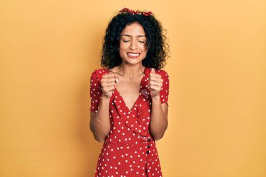 Young latin girl wearing summer dress excited for success with arms raised and eyes closed celebrating victory smiling. winner concept. 
