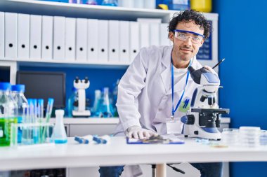 Genç İspanyol bilim adamı, laboratuarda mikroskop kullanarak belgeye yazı yazıyor.