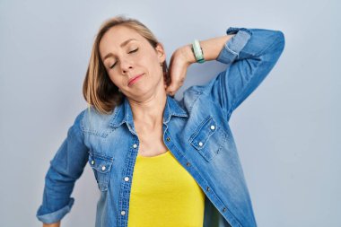 Mavi arka plan üzerinde duran genç sarışın kadın, yorgun ve rahat, uykulu ve sabahın erken saatleri için esniyor. 