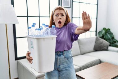 Elinde plastik şişelerle çöpleri geri dönüşüm sepetine koyan genç, kızıl saçlı bir kadın avuç içi hareketlerini durduruyor, kızgın ve hayal kırıklığına uğramış bir ifadeyle. 