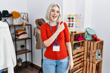 Young caucasian woman working as manager at retail boutique with a big smile on face, pointing with hand and finger to the side looking at the camera. 