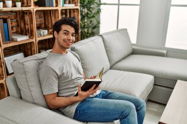 Evdeki kanepede oturmuş kitap okuyan genç bir İspanyol..