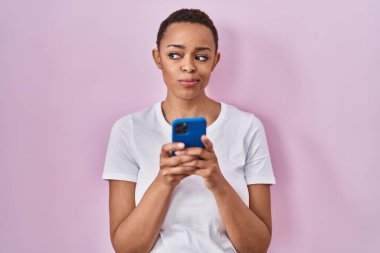 Güzel Afrikalı Amerikalı kadın akıllı telefon kullanıyor gülümsüyor ve yan tarafa bakıyor ve düşünüyor.. 