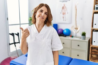 Orta yaşlı fizyoterapist kadın ağrı kesici kliniğinde çalışıyor. Elleriyle mutlu bir jest yapıyor. Kameraya bakıp başarıyı gösteren ifade. 