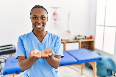 Black woman with braids working at pain recovery clinic smiling with hands palms together receiving or giving gesture. hold and protection 