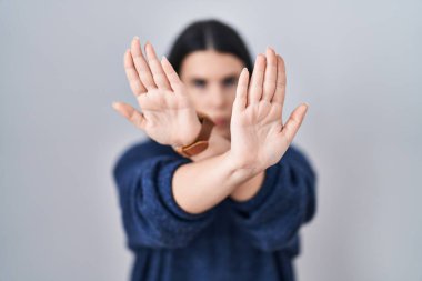 Genç esmer kadın izole edilmiş arka planda duruyor. Reddedilme ifadesi. Kollar ve avuçlar çapraz. 