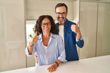 Middle age couple standing together doing happy thumbs up gesture with hand. approving expression looking at the camera showing success. 