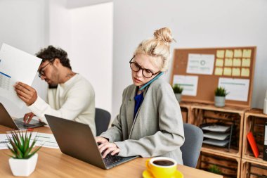 İki iş adamı akıllı telefondan konuşuyor ve ofiste dizüstü bilgisayar kullanıyorlar..