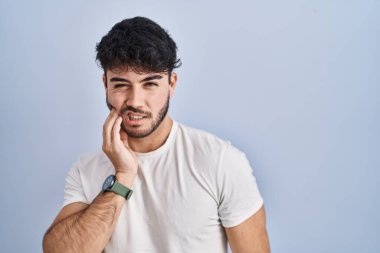 Hispanic man with beard standing over white background touching mouth with hand with painful expression because of toothache or dental illness on teeth. dentist 