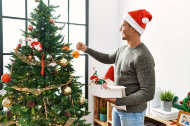 Genç İspanyol adam gülümsüyor. Evde kendine güvenen bir Noel ağacı süslüyordu.