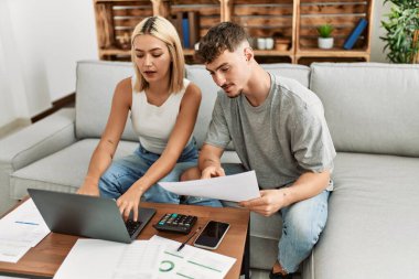 Evde dizüstü bilgisayar kullanarak aile ekonomisini kontrol eden beyaz bir çift gülümsüyor..