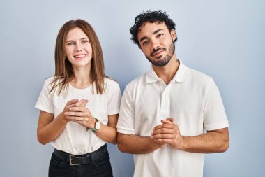 Gündelik giysiler giyen genç çift ellerini birleştirip gülümseyerek gevşemiş ve neşeli bir şekilde yan yana duruyorlar. Başarı ve iyimserlik 