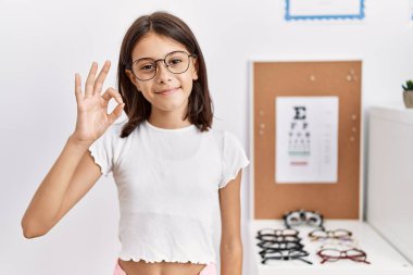 Gözlüklü genç İspanyol kız olumlu gülümsüyor. El ve parmaklarıyla 