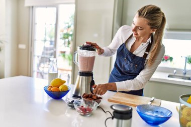 Genç sarışın kadın gülümsüyor. Kendine güveni tam. Smoothie 'yi sıvılaştırıyor.