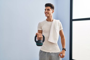 Genç İspanyol adam gülümsüyor spor merkezinde kettlebell kullanıyor.