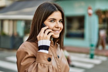 Genç, güzel, esmer bir kadın dışarıda mutlu bir şekilde gülümsüyor telefonda konuşuyor.