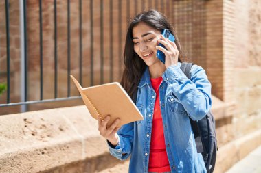 Genç İspanyol öğrenci kitap okuyor ve caddede akıllı telefondan konuşuyor.