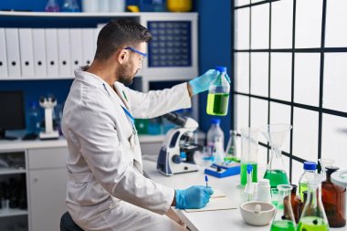 Laboratuardaki belgeye mikroskop kullanarak bilim adamı üniforması giyen İspanyol genç adam.