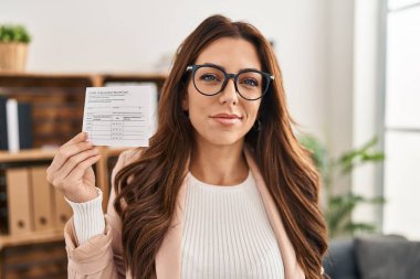 Genç esmer bir kadın elinde renkli bir kayıt kartı tutuyor. Olumlu ve mutlu görünüyor. Kendine güvenen bir gülümsemeyle dişlerini gösteriyor. 