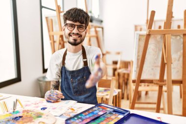 Hispanic man with beard at art studio smiling friendly offering handshake as greeting and welcoming. successful business. 