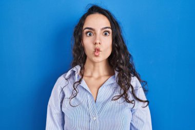 Mavi arka planda duran genç esmer kadın dudaklarıyla balık suratı yapıyor, çılgınca ve komik bir jest. Komik ifade. 