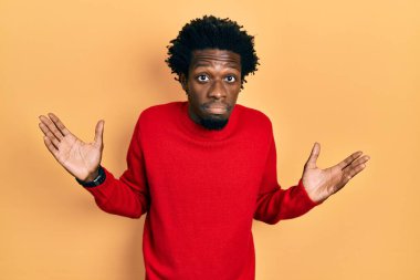 Genç Afro-Amerikalı sıradan kıyafetler giyen, habersiz ve kolları açık, hiçbir fikrim yok ve şüpheli bir yüzüm var.. 