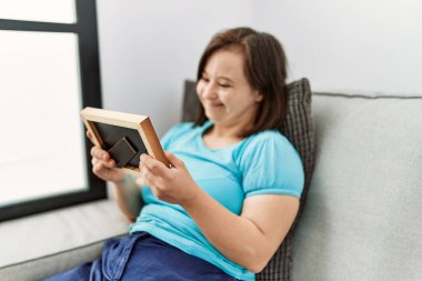 Brunette woman with down syndrome sitting on the sofa looking at frame at the living room