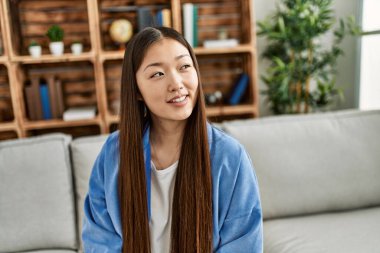 Genç Çinli kız gülümsüyor. Evdeki kanepede mutlu mesut oturuyor..