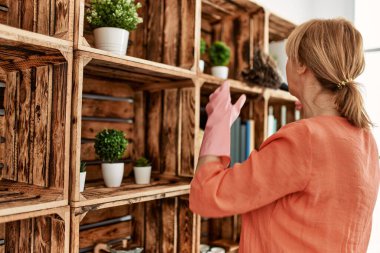 Orta yaşlı kadın evde toz bezi kullanırken mutlu bir şekilde gülümsüyor..