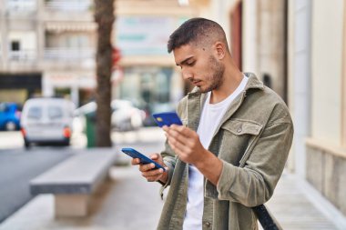 Genç İspanyol adam akıllı telefon ve kredi kartı kullanıyor.