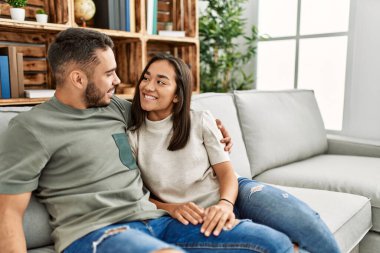 Kanepede oturan genç latin çift evde sarılıyorlar..