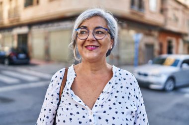 Orta yaşlı bir kadın sokakta kendine güvenerek gülümsüyor.